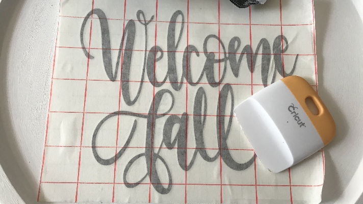 Adding the fall Cricut Design in vinyl to the pizza pan wreath